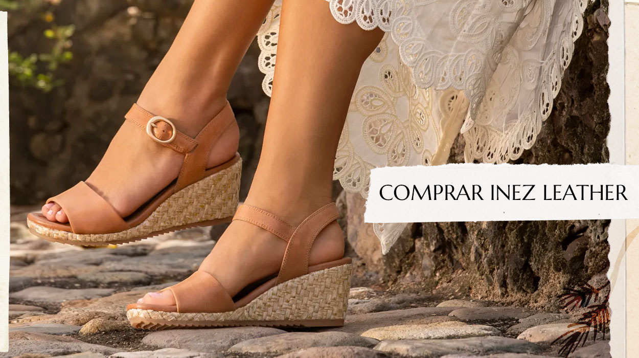 Mujer sentada con un vestido blanco, luciendo el modelo Inez de cuero en color tostado. Compra Inez Cuero.